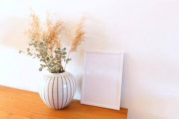 Blank photo frame, eucalyptus and dry reed in a vase. Modern Scandinavian style interior on the beautiful chest of drawers with white wall and bright room. Elegant interior. Summer, fall, still life.