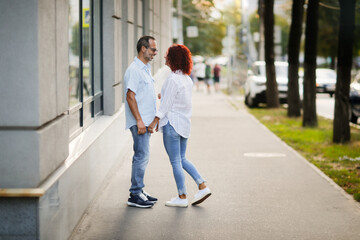 Cute European middle-aged couple holding hands walking in the city street, man and woman walking down the street in summer, back view