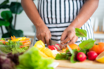 Vegetables and fruits such as mangos, lemons, bell peppers, tomatoes, carrots are prepared on the table and on a cutting board to cut, for salads in the kitchen.