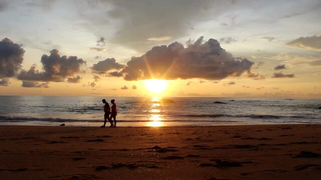 Silhouette of a couple taking a walk on a beautiful sandy sunset on the beach