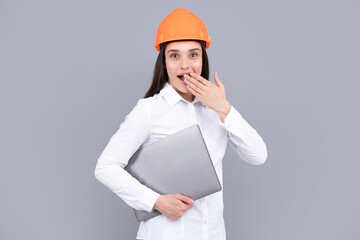 Surprised shocked excited business woman with laptop computer, portrait on gray. Portrait of female builder worker in hardhat helmet.