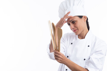 Young caucasian concerned chef in chef outfit while holding kitchen tools isolated on white background with copy space.