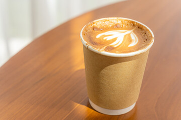 Hot coffee latte with latte art milk foam in cup made of paper on wood desk on top view. As breakfast In a coffee shop at the cafe,during business work concept