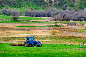 Fototapeta premium Old Tractor on Farm Field Green with Hills Mountains