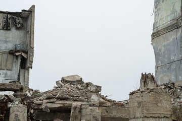 Gray debris of the building in the form of large concrete piles, slabs, beams with remnants of a brick wall against a gray sky. Background