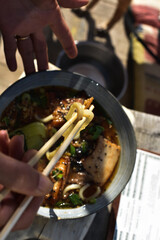 A hand holding two Japanese sticks  over a plate full of vegetable soup.Thai style of eating vegetables.Thai-made vegetable soup.