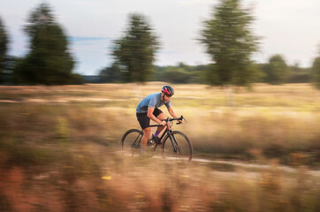 Fototapeta na wymiar Cyclist in motion. Young sporty man rides gravel bike along the trail in the field. Blurred motion. Sport and travel.
