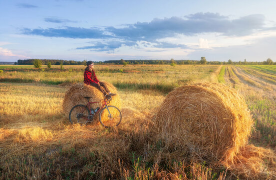 Cyclist sits on a haystack after a bike ride at sunset. Active lifestyle and travel concept.