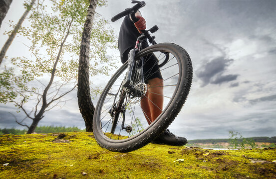 Cyclist stands with a bicycle on a rock overgrown with moss. Low angle view. Sport and travel outdoors.
