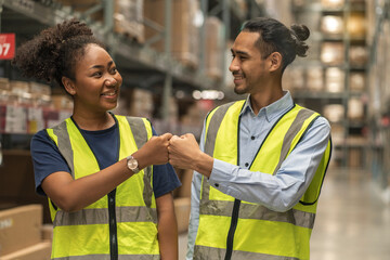female African American employee and an Asian employee wearing a uniform hifive greet each other and work together to inspect goods in the warehouse. © supAVADEE BUTRADEE