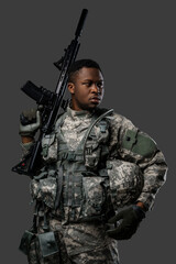 Combative african soldier with serious face holding rifle on his shoulder against dark background.