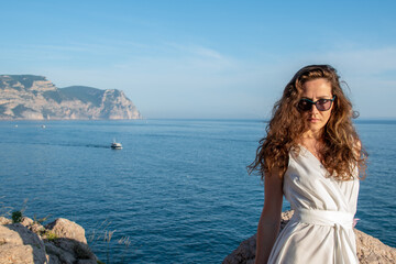 Fototapeta na wymiar Stylish bride standing back with wedding bouquet on beautiful landscape of sea and mountains on sunset