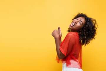 laughing african american woman showing thumbs up and looking at camera isolated on yellow.