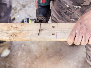 Close-up of a man cutting a plank of wood with a jig saw. Selective focus.