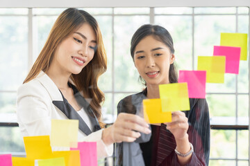 Group of business Asian women meeting at the office and use post it notes on glass wall. Business...