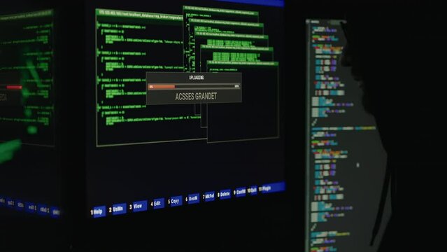 Silhouette of professional hacker in hoodie using computer with binary codes while sitting in dark room. Male web genius getting access into data center during cyber attack.