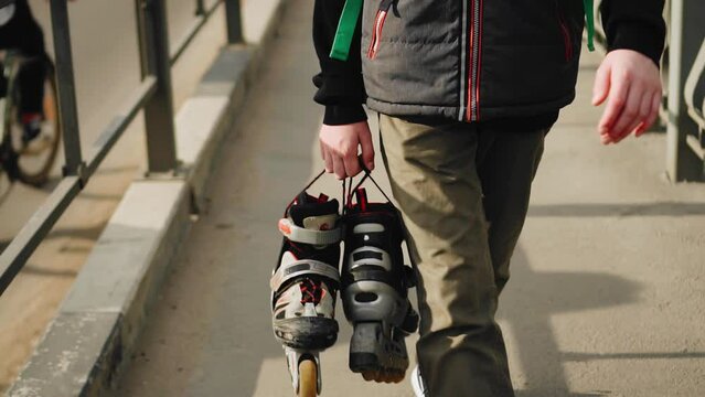 A guy walks with roller skates in his hands after skating. Shooting close-up in slow motion