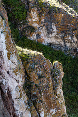 Hillside with rocky cliffs on sunny day. Autumn weather, yellow trees in forest. Basalt stones protrude to surface, formation of karst caves and gorges