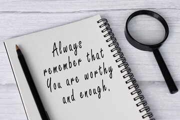 Motivational quote on note book with magnifying glass on white wooden desk.
