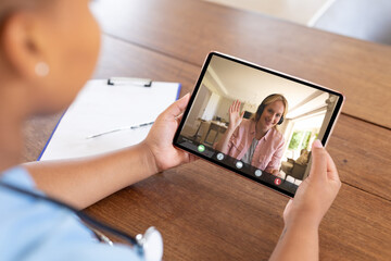 Fototapeta na wymiar African american female doctor talking to caucasian female patient on video call over digital tablet