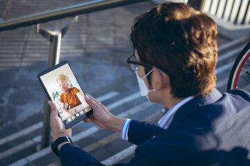 Asian businessman wearing mask during video call with albino african american male colleague