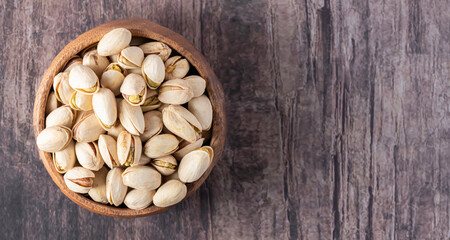 Pistachios in a wooden bowl, isolated on a marble background, overhead view. space for text