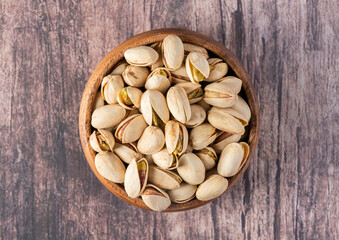 Pistachios in a wooden bowl, isolated on a marble background, overhead view.