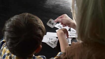 Mom teaches her son how to say the words on the cards at home at the table