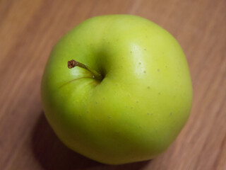 One apple of Golden cultivar on a wooden surface. Close-up shot.