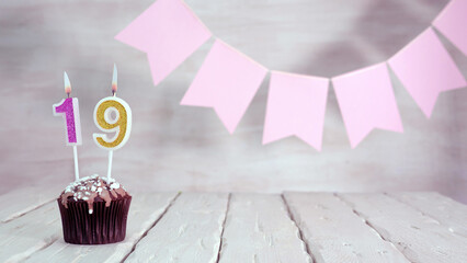 Birthday number 19. Festive background for a girl or woman with a muffin and candles burning pink...