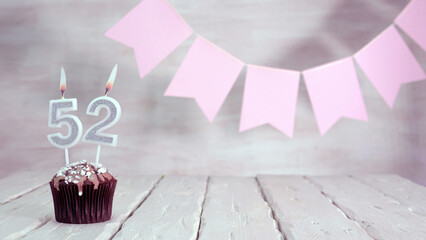 Birthday number 52. Festive background for a girl or woman with a muffin and candles burning pink...