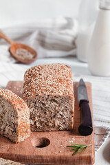 Fresh sliced sesame bread on wooden board, rosemary, knife and milk bootle. Healthy eating concept. Gluten free bread.