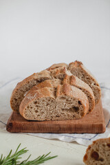 Fresh sliced rye bread close up on a wooden board, knife and rosemary on a white background. Side view. Copy space.