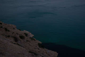 View from high on the quiet expanse of the blue water of the sea. Rocky coast.