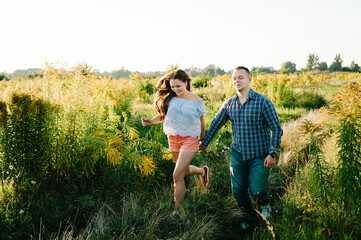 Naklejka na ściany i meble Romantic man and woman walking on field on nature enjoying sunlight. Concept of lovely family holding hands. Young couple walk on grass the country.