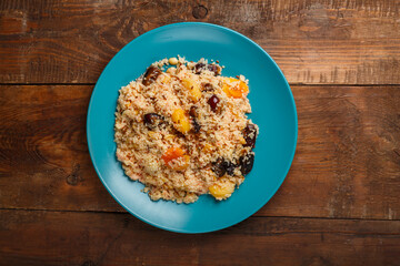 A large dish of couscous with dried fruits, saffron and nuts on a wooden table.