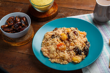 a plate of couscous with dried fruits and nuts on a wooden table with a wooden spoon next to dates and cereals.