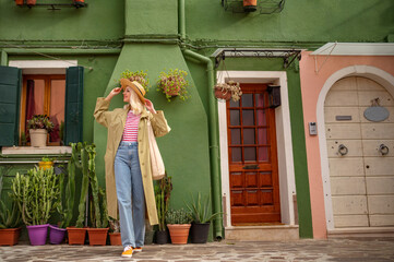 Happy smiling traveler woman wearing stylish outfit posing, walking  near green color house. Copy,...