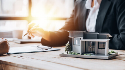 A model of a small house sits on a library in one of the housing estate showrooms, a sample house project where a salesperson advises customers. The concept of selling houses in the project. - obrazy, fototapety, plakaty