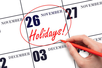 Hand drawing a red circle and writing the text Holidays on the calendar date 26 November. Important date.