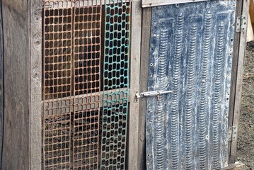 one metal latch on a black old door and a rusty iron wall with metal mesh