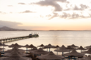 Fototapeta na wymiar Mediterranean coast with sunbeds and straw sun umbrellas on the sandy beach