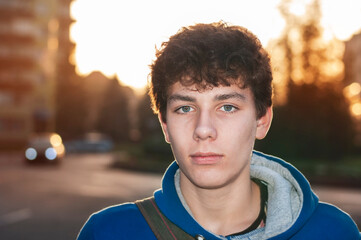 The teenage boy returns from school in the city, happy but tired after mental work in class. Portrait of teenage high school student boy at sunset