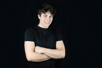 On a dark background portrait of a happy teenage boy with a beautiful smile, his beauty and grace and strength stand out well on a dark background, a place for text and advertising