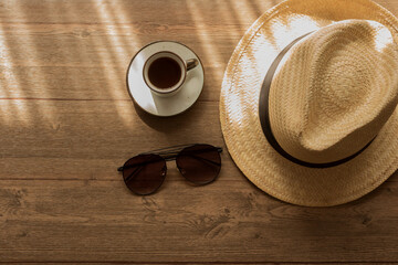 Lentes obscuros, café  y sombrero en mesa de madera
