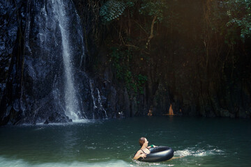 Travel and nature. Young woman swimming in tropical waterfall pool.