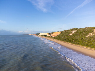 Amazing land cliffs with the golden hour of the rising sun and beautiful beach in Parrancho, Arraial da Ajuda, Bahia, Brazil, South America. Aerial drone view.