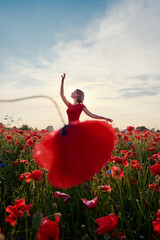 Pretty young woman in red dress dancing like ballerina in the poppy flowers meadow.