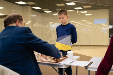 Concentrated boy develops a chess strategy, plays a board game with adult professor .Chess game in action. Board in details. 