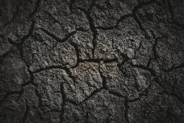Black dried cracked earthen soil, background texture